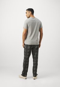 Grå kortærmet T-shirt kombineret med sorte bukser med slangeprint og hvide sneakers. Sættet har en afslappet pasform og tekstureret stof.