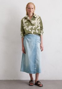 Green floral-print button-up shirt with long sleeves, paired with a light blue denim wrap skirt. Black slide sandals with a gold buckle detail.