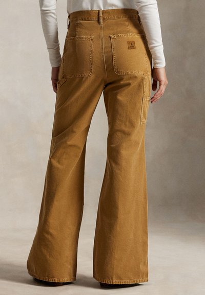 Rjave flared hlače iz korduroja z dvema zadnjima žepoma, vidnimi šivi in etiketo na desnem žepu. Gladek tekstura in prilagojen kroj.