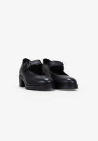 Zapatos Mary Jane de cuero negro con punta redonda, tacón grueso y correa ajustable con una hebilla metálica redonda.
