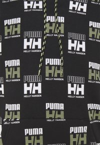 Felpa nera con cappuccio caratterizzata da ripetuti logo "PUMA" e "Helly Hansen" in bianco e verde neon. Tessuto testurizzato con lacci a contrasto.