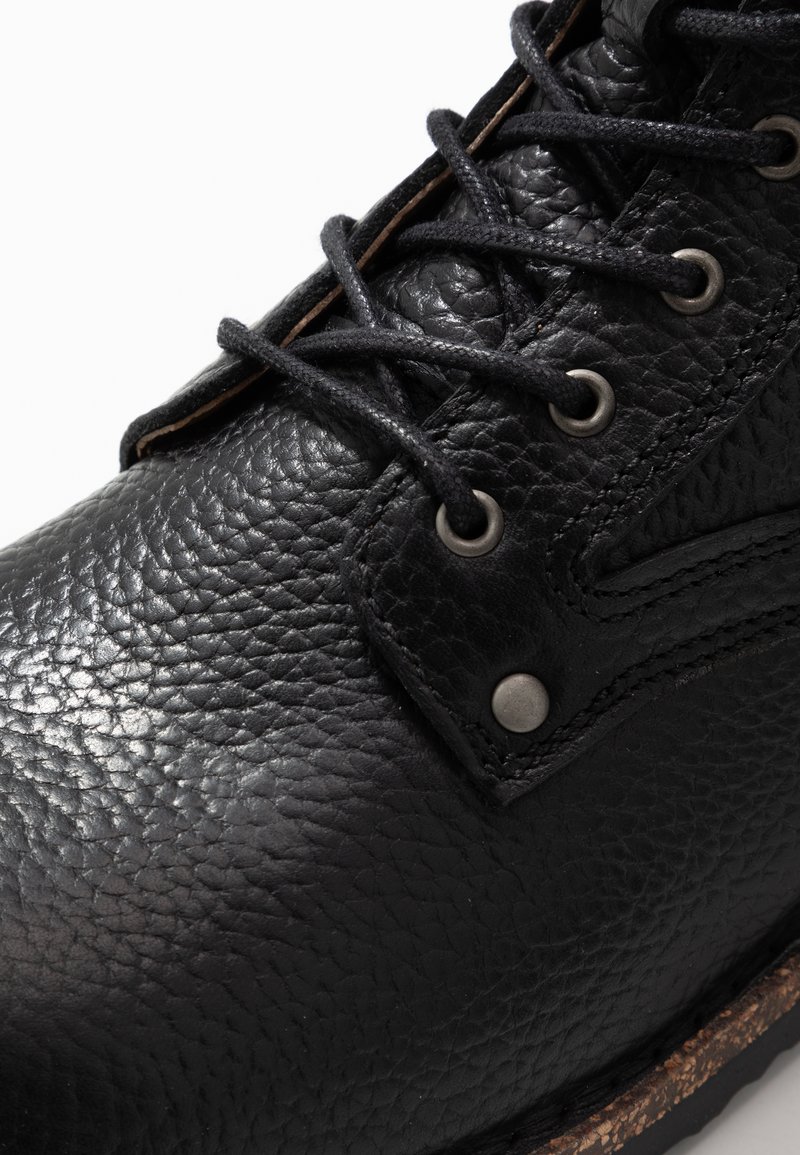 Stivale in pelle nera con finitura testurizzata, design con lacci rotondi, occhielli in metallo e suola simile al sughero. Dettagli di cucitura evidenti.