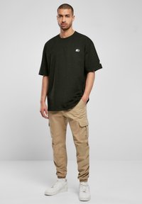 Black oversized t-shirt with a small logo, paired with beige cargo pants and white sneakers with textured detailing and laces.