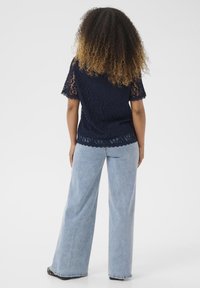 Top in pizzo blu navy con maniche corte a scalloped, abbinato a jeans a gamba larga leggeri a vita alta. Tessuto morbido, motivo floreale, design elegante.
