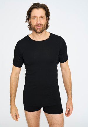 Schwarzes kurzärmliges Hemd aus glattem Stoff, mit Rundhalsausschnitt und taillierter Passform, kombiniert mit schwarzen enganliegenden Shorts, die eine klare Silhouette zeigen.