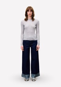 Haut à manches longues gris clair à côtes, associé à un jean bleu foncé à jambes larges avec un ourlet retroussé. Chaussures argentées. Design simple et minimaliste.