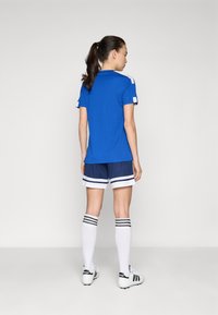 Blå idrottströja med korta ärmar och vita detaljer, kombinerad med marinblå shorts med vita ränder och knähöga vita strumpor med svarta ränder.