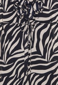 Blusa a righe zebra blu navy e crema con scollatura arricciata, chiusura con bottoni davanti e dettaglio con coulisse in vita. Tessuto morbido al tatto.