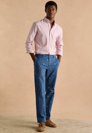 Hellrosa gestreiftes Hemd mit Knöpfen, blaue Hose mit kleinen Segelbootmustern und braune Schnürschuhe. Glatte Stoffe, maßgeschneiderte Passform.