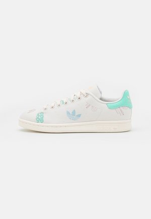 Baskets basses blanches avec logo bleu clair et languette de talon bleu sarcelle, semelle cousue et lacets blancs.