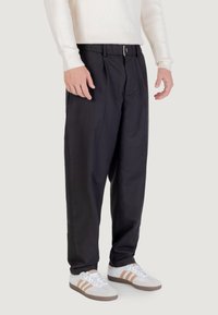 Czarne tapered spodnie o gładkiej teksturze, z zapięciem na guzik i plisami. Połączone z białymi sneakerami z brązowymi akcentami.