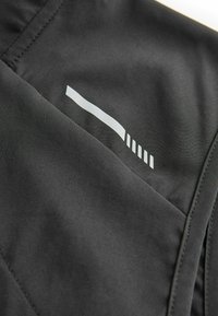 Un tissu noir au toucher lisse présente un motif blanc réfléchissant, comprenant une ligne horizontale et des rayures verticales près de la couture.