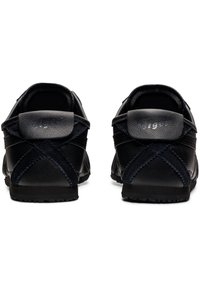 Black athletic shoes with a leather and suede upper. Rear view shows a cross-stitched design and textured heel accent. Rubber sole.