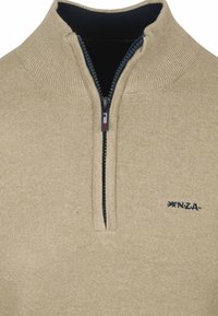 Beige ritsvest met opstaande kraag, voorzien van een donkerblauwe binnenvoering en het N.Z.A. logo in het donkerblauw geborduurd op de borst.