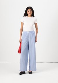 Bílá tričko a modré pruhované široké kalhoty s elastickým pasem. Červená kabelka a černé boty s dekorativními akcenty. Jednoduchý, neformální outfit.