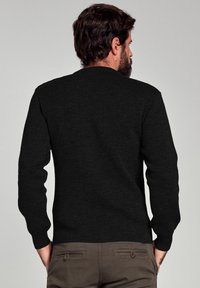 Pull noir à manches longues, col rond et texture lisse. Design simple sans motifs ni accents visibles.
