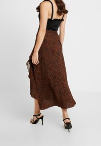 Jupe maxi en tissu à imprimé animal orange et noir. Ourlet asymétrique avec une texture fluide. Associée à un top noir et des talons noirs à lanières.