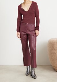 Bordowy prążkowany sweter z głębokim dekoltem w kształcie litery V i srebrnymi akcentami, zestawiony z bordowymi skórzanymi spodniami o prostych nogawkach oraz metalicznymi botkami za kostkę.
