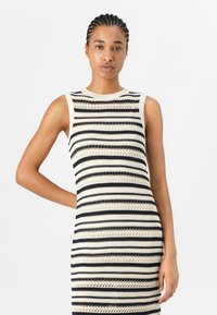 Robe sans manches en tricot avec des rayures horizontales alternées bleu marine et crème, motifs ajourés complexes et coupe ajustée.