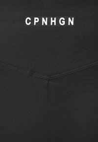 Black athletic leggings feature a smooth, matte texture with a white logo "CPNHGN" centered near the waistband and reinforced stitching along edges.
