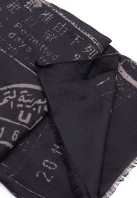 Bufanda negra hecha de un tejido suave, con un diseño impreso que presenta texto gris claro y patrones abstractos, bordes sin acabar y forma cuadrada.