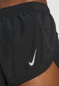 Pantalones cortos deportivos negros con paneles laterales de malla, cintura elástica y un logo plateado de la marca Nike en la parte frontal inferior.