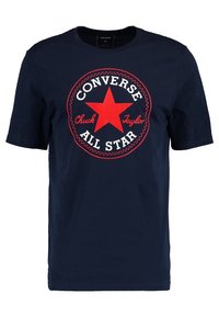 Camiseta de algodón azul marino con un gran logo de estrella roja que lleva el texto "Converse Chuck Taylor All Star" en blanco y rojo. Mangas cortas, cuello redondo.