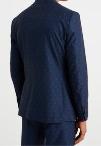 Navy blazer with a tailored fit, featuring subtle gold dot patterns, peak lapels, and buttoned cuffs. Smooth fabric texture.