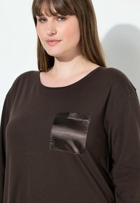 Maglietta marrone a maniche lunghe, con una tasca in satin e una scollatura ampia. Tessuto morbido con una vestibilità comoda e una trama liscia.