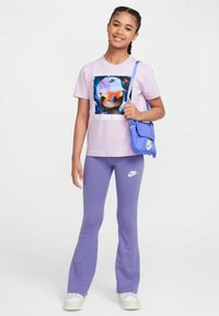 Pantalones largos morados y una camiseta rosa claro con un gráfico colorido de un animal usando una gorra y gafas de sol. Bolsa azul con el logotipo de Nike.