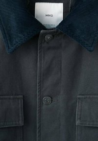 Donkergrijze jas met een navyblauwe corduroy kraag, twee zijzakken en een zwarte knoop. Etiket zichtbaar in de kraag.