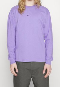 Långärmad lila Nike t-shirt med rundad halsringning och broderad logotyp på bröstet. Tyget verkar mjukt och lätt.