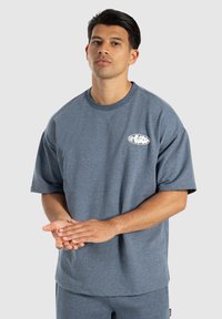 Grå kortærmet T-shirt med en afslappet pasform, der har et lille hvidt logo på venstre bryst, lavet af blødt, tekstureret stof.