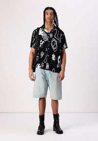 Kortermet svart skjorte med hvite abstrakte mønstre, kombinert med lyseblå denimshorts og svarte støvler, med en avslappet passform.