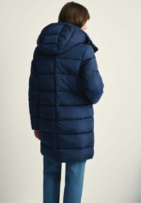 Granatowa puchowa kurtka z kapturem, z pikowanym wzorem i długim krojem, prezentowana z tyłu. Miękka, gładka tekstura.