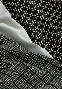 Tre pezzi di tessuto: uno grigio, due neri con motivi geometrici bianchi—piccole quadrati e forme romboidali più grandi con accenti cuciti.