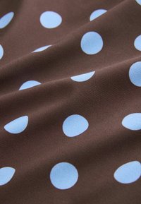 Tissu marron avec de grands pois bleu clair uniformément espacés, présenté avec de doux plis et une texture visible.