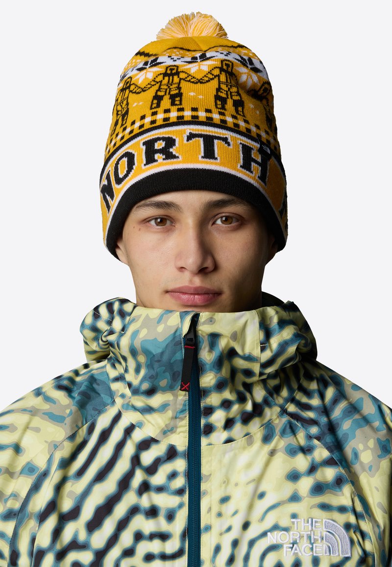 Knit beanie w kolorze żółtym z czarnymi akcentami, ozdobiony fantazyjnymi wzorami i pomponem na czubku. Kurtka z kapturem w wielokolorowe abstrakcyjne wzory.