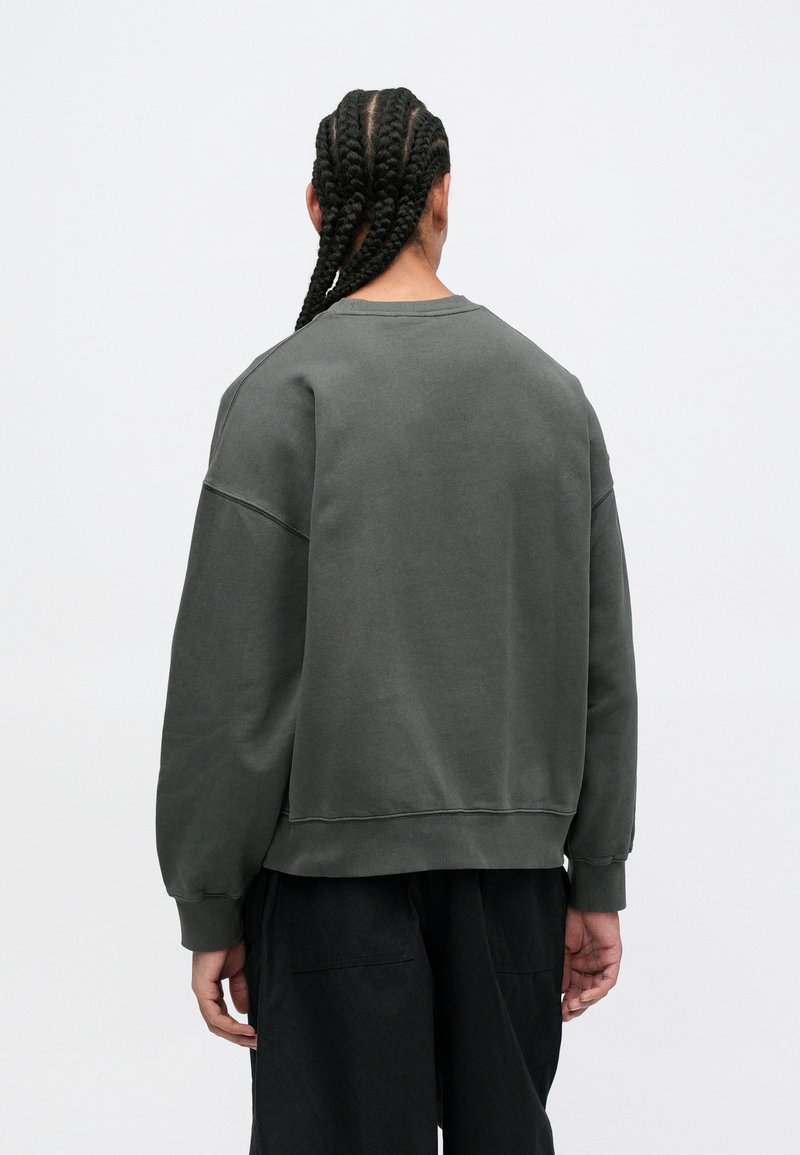 Sudadera verde oscuro con un ajuste relajado, puños acanalados y cuello redondo. Fabricada con una tela suave, cuenta con hombros caídos y un diseño liso.