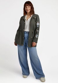 Olivgrön jacka med blommig broderi, framfickor och guldfärgade detaljer. Matchad med ljusblå vida jeans och vita sneakers.