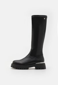 Bota negra de cuero hasta la rodilla con punta redonda, suela de goma gruesa y acento plateado en el tacón. Textura suave y diseño aerodinámico.