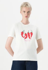 White cotton t-shirt featuring red chili pepper graphics with green stems and pink text saying "SPICE IT UP". Short sleeves, crew neck design.