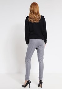 Černý oversized svetr, šedé kalhoty s úpravou na míru a černé vysoké podpatky. Hladký materiál, uvolněný střih, s diskrétními detaily kapes na kalhotách.