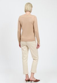 Maglione lavorato a maglia di colore marrone chiaro con maniche lunghe, orlo a coste, abbinato a pantaloni beige alla caviglia e scarpe basse marroni con tacco. Texture liscia.