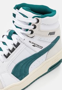 Baskets montantes Puma Slipstream blanches et bleu sarcelle avec accents en suède et lacets blancs, vues de côté.
