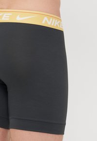 Svarta idrottsshorts med en gul midja och vit "NIKE"-logotyp, tillverkade av ett mjukt, stretchigt material. Slut på byxorna vid mitten av låret.
