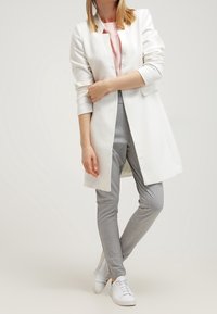 Blazer bianco lungo su una maglietta rosa chiaro, pantaloni grigi aderenti e sneaker bianche. Tessuto morbido, vestibilità su misura e linee pulite.