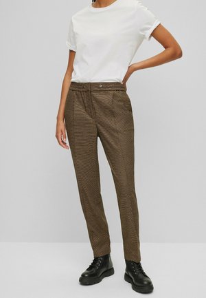 Pantalons bruns à motif avec une coupe décontractée, présentant une taille plate, des poches latérales et une ceinture lisse. Associés à un T-shirt blanc à manches courtes.