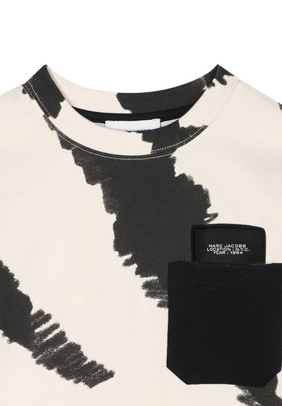 Korte mouwen shirt in crème met gedurfde zwarte abstracte patronen, voorzien van een zwarte zak met een logo label waarop "Marc Jacobs, NYC 1984" staat.