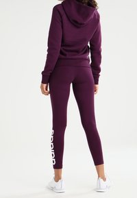 Conjunto deportivo morado con sudadera con capucha y leggins a juego. Los leggins tienen el logo blanco de "adidas" en la parte inferior de la pierna.